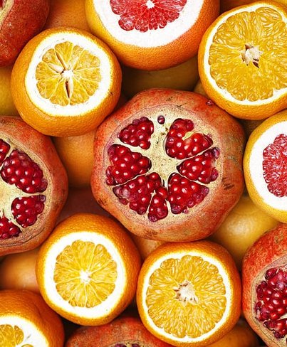 massa citrusfrukter ligger på varandra och tillsammans, grapefrukt, granatäpple och apelsin. De frukter som ligger högst upp är skurna i mitten med fruktköttet liggandes uppåt.